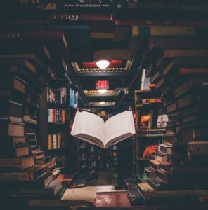 creative writing - a book floats infront of library stacks of books